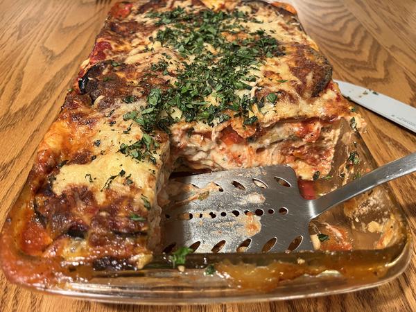 A baking dish containing a beautiful lasagna. A large piece has been cut out, and its place is a metal spatula.